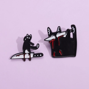 Detail showing two black cat enamel pins with spooky knife designs on purple background