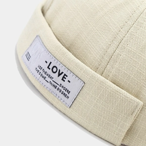 Beige twill fabric docker cap with woven label detail shown from a side profile angle