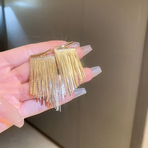 Macro shot of long gold metallic chain fringe earrings held by hand with sparkling effect