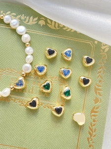 Detail of 18k gold heart charms with colorful stones on vintage book and silk