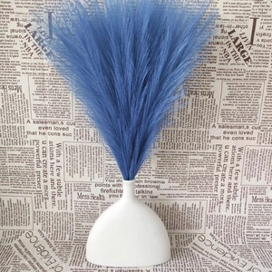 Blue artificial pampas grass bouquet in a white ceramic vase with vintage paper backdrop