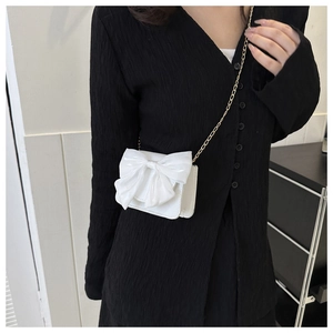 Detail view of a cute white crossbody bag featuring a large gauze bow and chain strap.