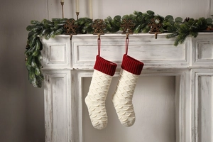 Detail of knitted Christmas stockings with red cuffs and fish-scale texture on a white mantel