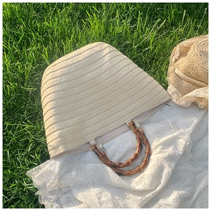 Detail of hand-woven straw tote with natural bamboo handles on a lace mat outdoors