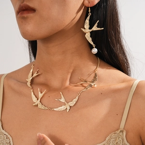 Detailansicht der goldenen Schwalben-Halskette und passender Perlenohrringe am Model