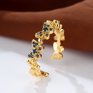 Detailed close-up of golden butterfly ring with blue crystals on a reflective surface