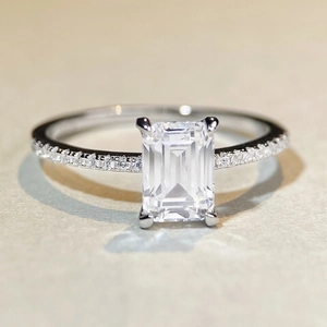 Macro shot of emerald cut moissanite ring with side diamonds on polished silver band
