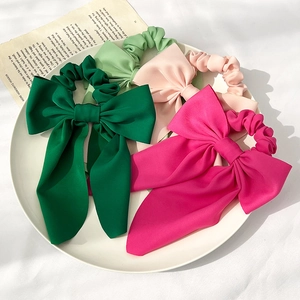 Draufsicht auf vier Satin-Haargummis mit Schleife in Grün und Rosa auf einem weißen Teller