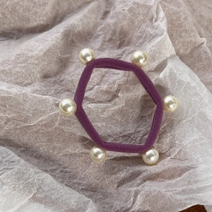 Close-up of a purple elastic hair tie featuring six white pearls on textured background