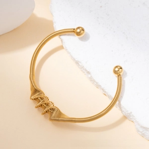 Detail view of gold titanium steel twisted bangle on white rock showing refined metal texture
