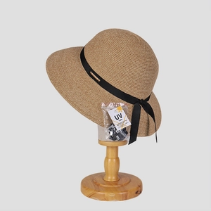 Elegant wide brim straw sun hat with black bow and UV protection tag on wooden stand