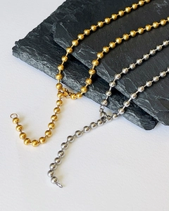 Detail of gold and silver beaded metal ball chains displayed on a textured stone piece