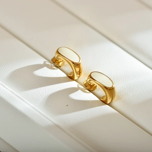 Macro shot of U-shaped gold-plated earrings with smooth off-white enamel finish details