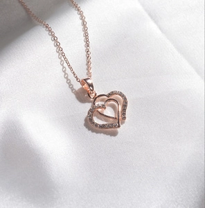 Macro shot of rose gold double heart pendant with cubic zirconia on silk fabric