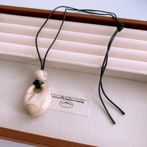 Detailed shot of a vintage marble-patterned pendant on a minimalist black cord necklace