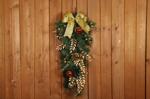 Christmas teardrop swag with green pine needles, gold bow, and festive ornaments on wood
