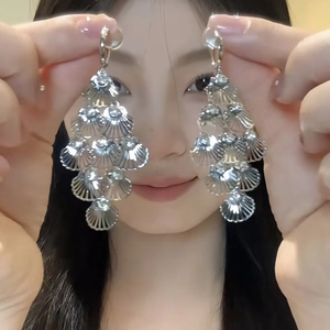 Detail of oversized silver layered shell drop earrings showing ribbed texture on a model