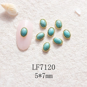 Détail d'un bijou d'ongle turquoise 5x7mm avec cadre doré perlé sur peluche blanche