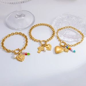 Three gold stainless steel bracelets with heart charms, pearls, and cross pendants on glass