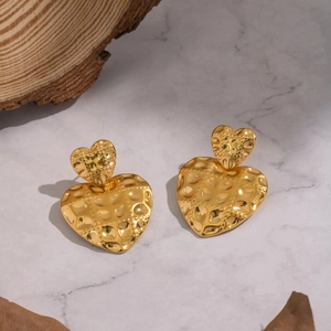 Detailed view of vintage gold heart earrings with hammered texture on marble surface