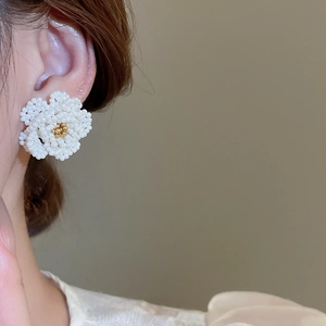 Detailed close-up of handmade camellia pearl beaded flower earrings on a model