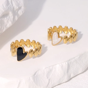 Close-up of adjustable gold heart rings with black and white enamel on stone texture
