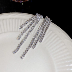 Close-up of sparkling long tassel earrings with rhinestones on a white ceramic plate