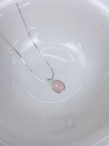 Nahaufnahme eines rosa Chalcedon-Anhängers an einer S925-Silberkette in einer Keramikschale