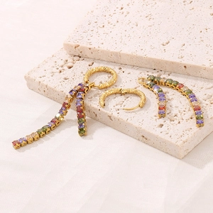 Macro shot of gold tassel earrings featuring multi-color zircon stones on a beige stone