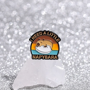 Macro shot of Capybara enamel pin with 'I NEED A LITTLE NAPYBARA' text on crystal rock
