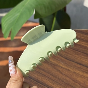 Medium matte sage green claw clip held by hand against a wooden and leaf background