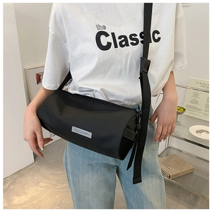 Détail d'un sac bandoulière de sport cylindrique noir porté pour montrer la taille réelle