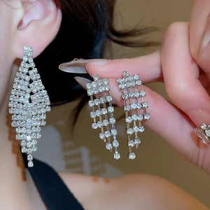 Detail of silver V-shaped tassel earrings with clear rhinestones on model's ear