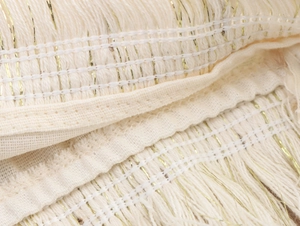 Macro view of cream cotton fabric with gold thread accents and tassel fringe detail