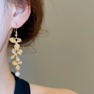 Detailed close-up of matte gold flower drop earrings with a pearl accent on a model