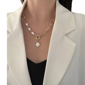 Asymmetric gold chain necklace with Baroque pearls worn over a white suit and black top