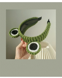 Detail of green knitted frog headband with large eyes and non-slip inner teeth