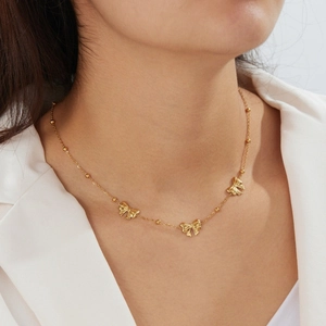 Detailed close-up of a gold-plated beaded chain necklace with three elegant butterfly pendants