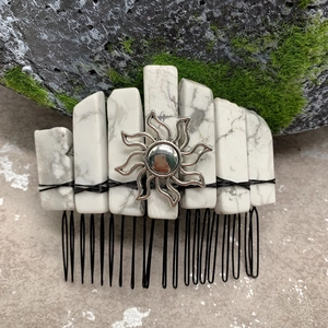 Macro shot of white marble crystal hair comb with silver sun charm on mossy stones