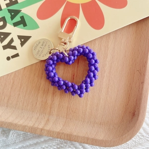Macro detail of handmade purple pearl heart keychain with golden metal clasp on wood