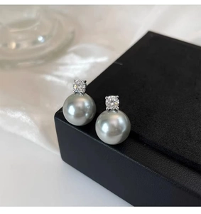 Detailed view of gray pearl stud earrings with sparkling zircon on a black jewelry box