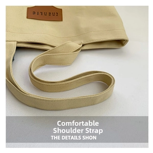Detail of minimalist canvas tote bag with woven strap and embossed leather logo patch