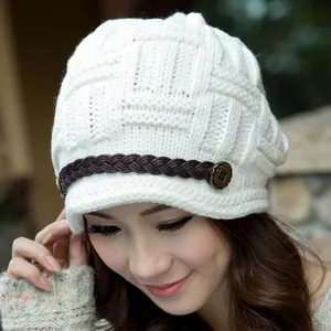 Close-up of cream knit winter hat featuring cable texture and brown leather strap detail