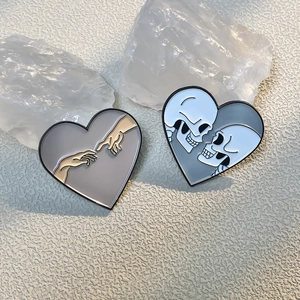 Detail of heart enamel pins showing Adam hands and skulls on stones background