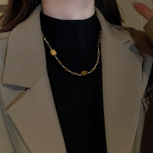 Détail du collier de perles en œil de tigre et perles dorées sur un pull noir chic