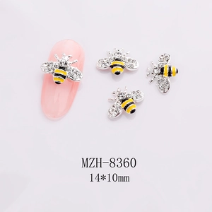 Macro detail of 3D bee nail charms with yellow enamel and white rhinestones on pink nails