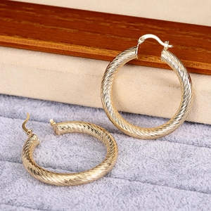 Dettaglio di orecchini a cerchio dorati con texture a spirale e chiusura a scatto