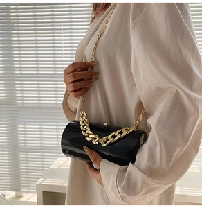 Detail of a black cylindrical acrylic crossbody bag with chunky gold chain strap