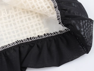 Détail macro du tissu noir et de la maille beige reliés par des coutures blanches