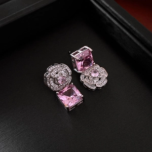 Close-up of silver earrings with pink zircon flower and square gemstones on black background